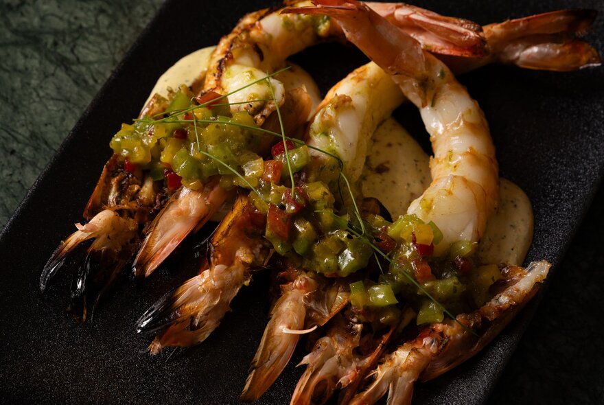 A plate of grilled prawns with a green salsa on top.