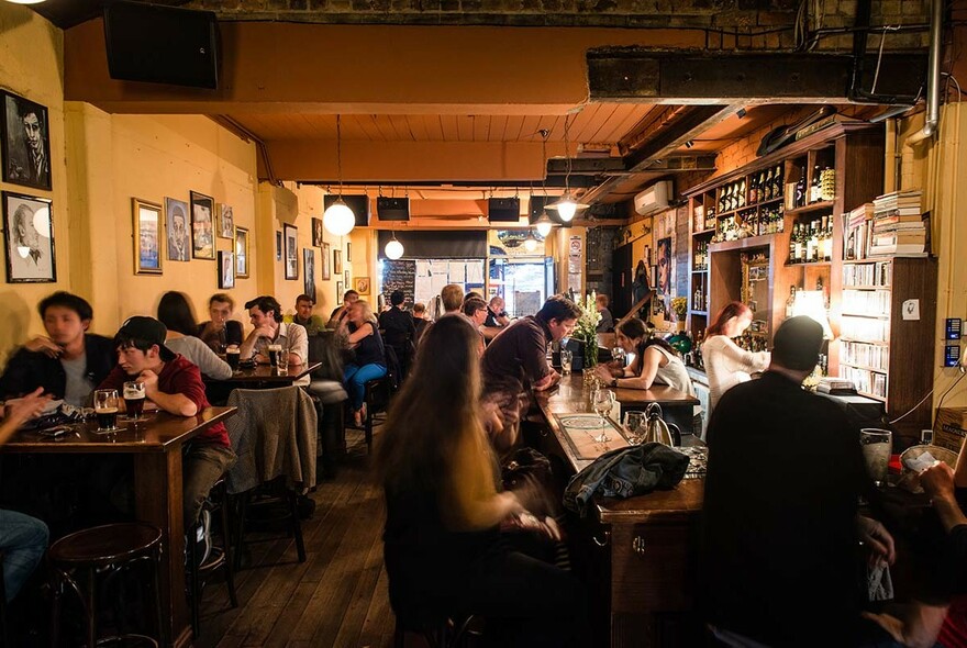 Interior showing a crowded bar, with people sitting at tables, people waiting at bar counter for service.