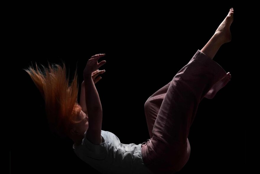 Art photograph of a person falling onto their back, their legs and arms raised.