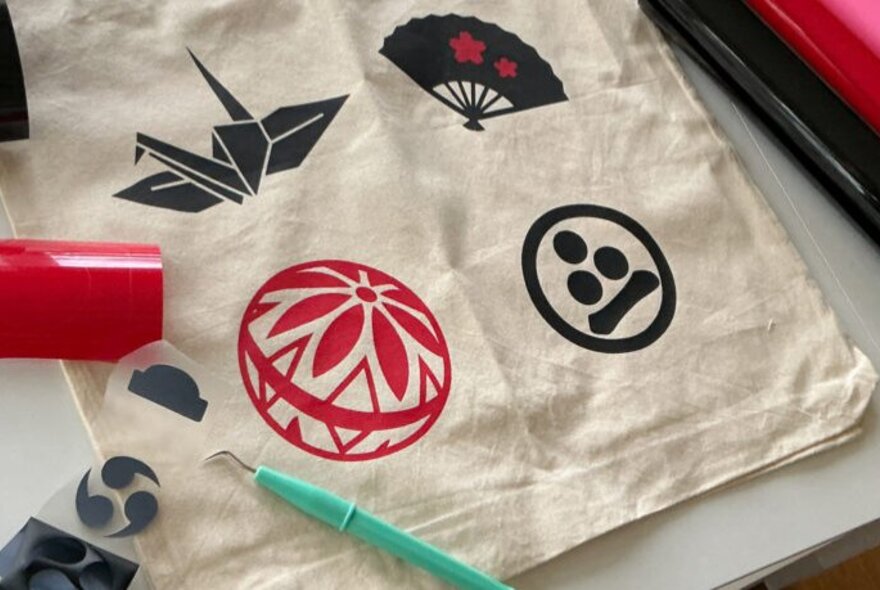 A calico bag printed with stamped designs in red and black ink, with craft tools on the table.
