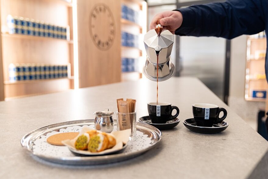 Hand pouring coffee into cups next to a plate with two cannoli.