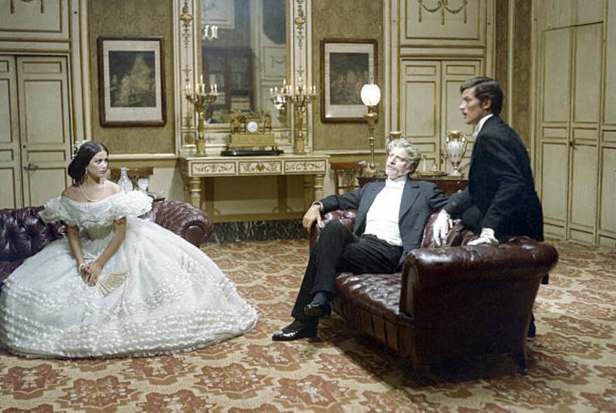 A still from the film The Leopard, with the three actors dressed in clothing from the 1880s in an ornate parlour setting.