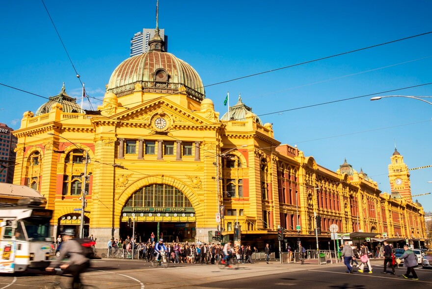 Red and yellow brick historic Flinders Street Railway Station with a dome and series of clocks.