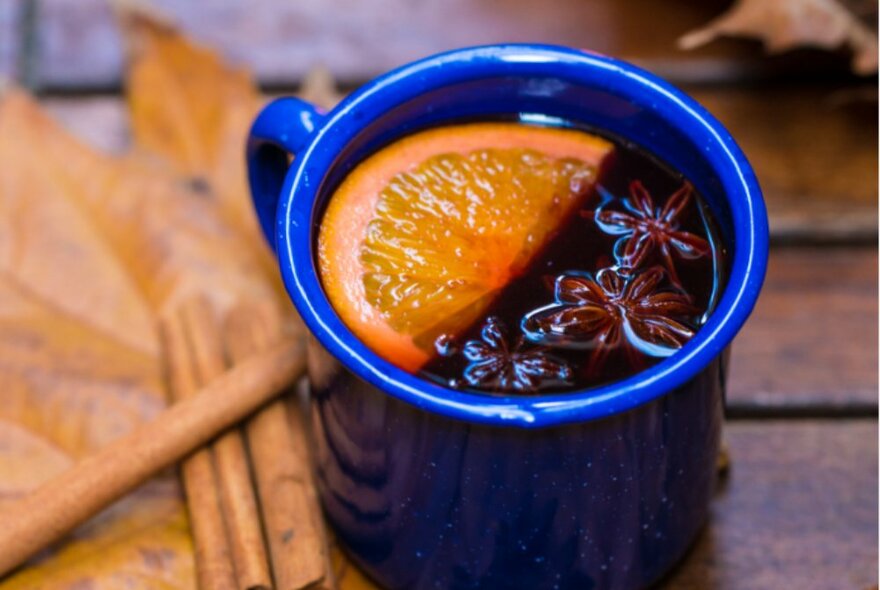 A blue mug filled with mulled wine, star anise and an orange wedge.