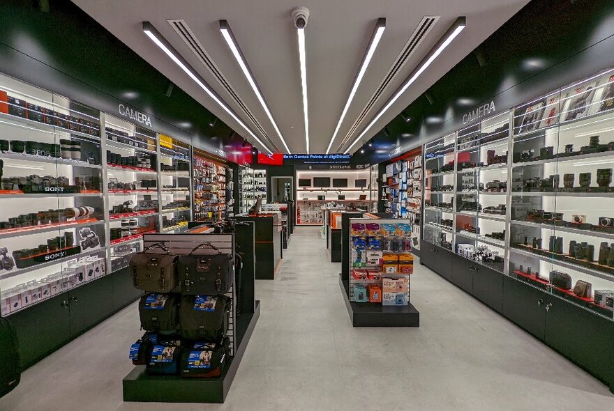 Long interior view of digital store with backlit shelves displaying products.