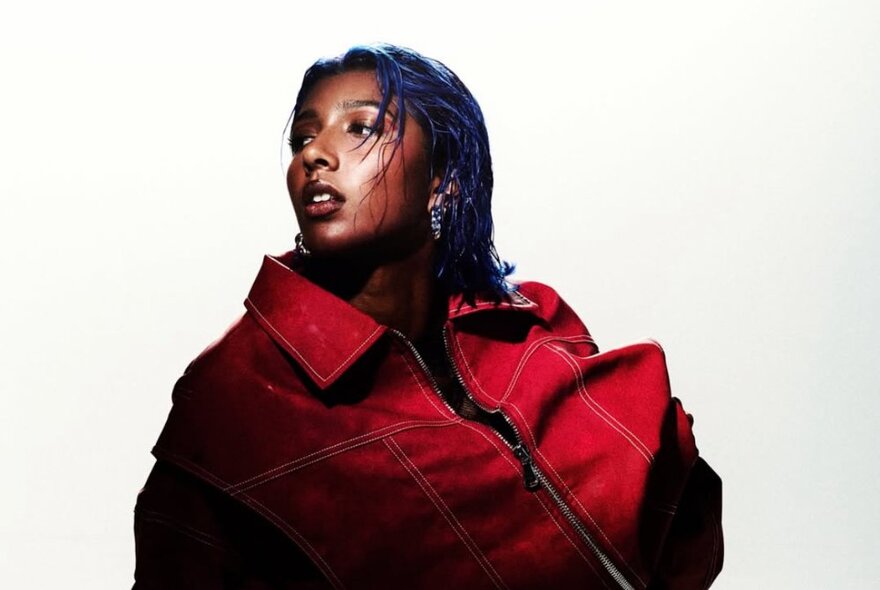 Singer Charlotte Dirckze posing for the camera against a white background, wearing an oversize red jacket.