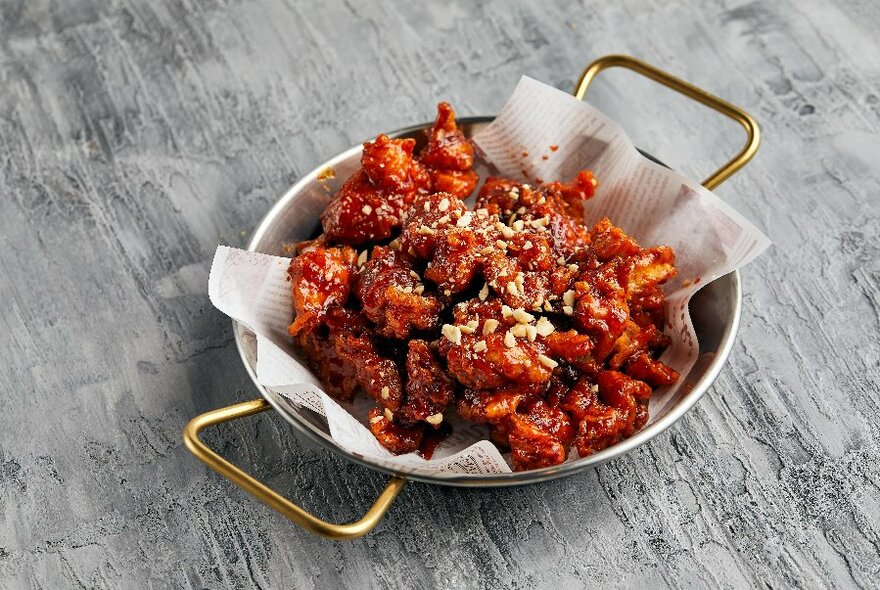 A bowl of fried chicken coated in red sauce