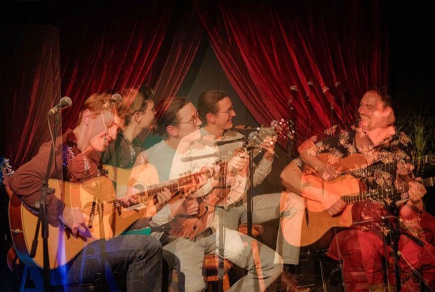 Three seated musicians on stage playing guitars, the time-lapse capturing multiple images of each of them.