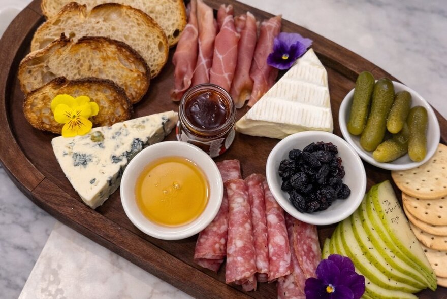 A charcuterie board of wedges of cheese, sliced cured meats, bread, olives and pickles, served on a wooden platter.