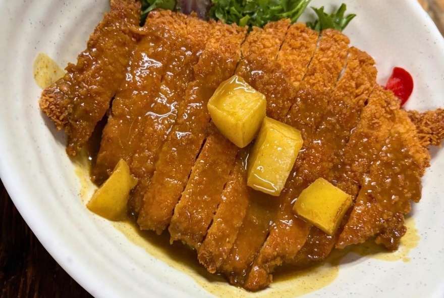 Looking down on a plate of Katsu chicken with yellow cubed garnish. 