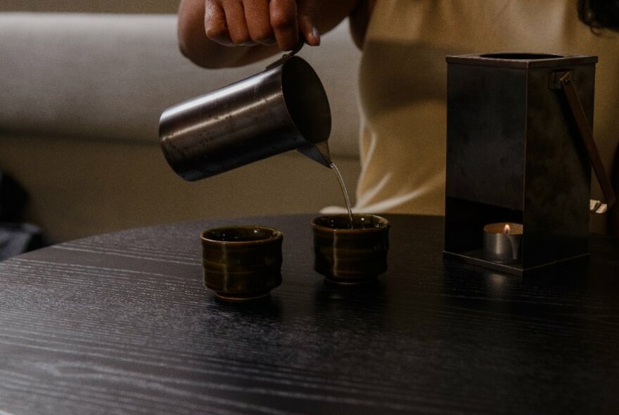 Bartender pouring liquid into cups on a wooden counter.