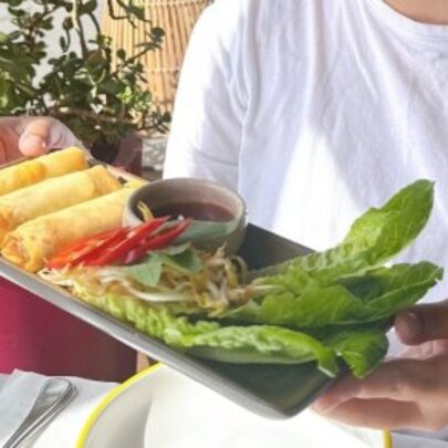 Person holding tray of spring rolls and garnish.