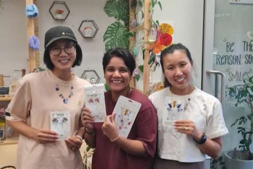 Three smiling workshop participants in a studio space, holding up jewellery they have made.