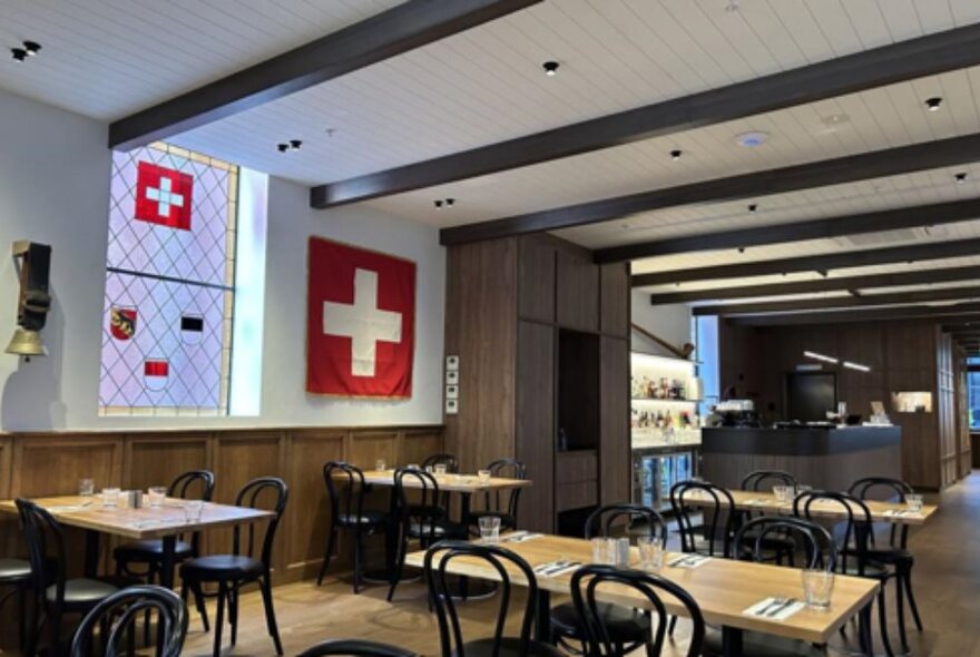 Swiss dining cafe with Swiss flags, timbered ceiling, tables and chairs and wood details.