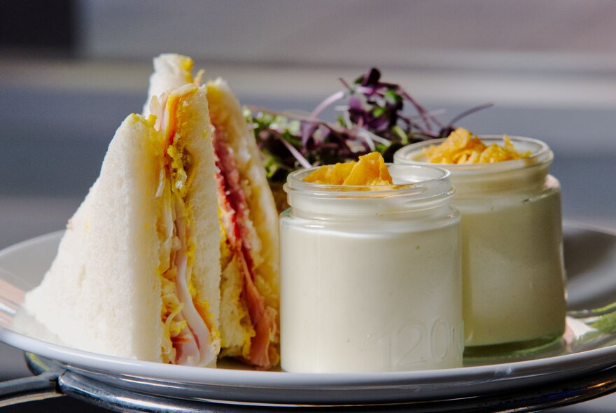A plate with small sandwiches and jars or panna cotta.