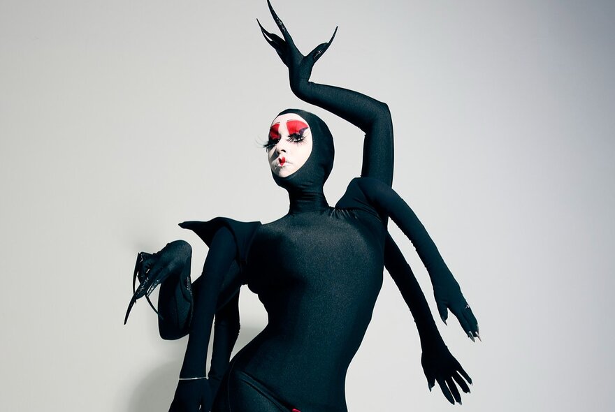 A woman in a tight black spider costume, with four extra 'arms' and face heavily made up with white, red and black makeup.