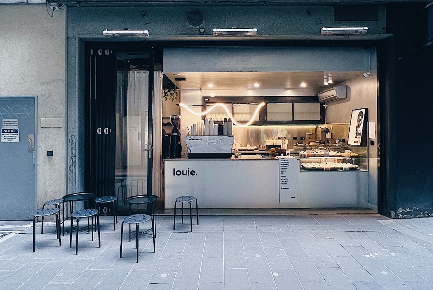 A small modern-looking cafe with a few small tables and chairs out the front. 