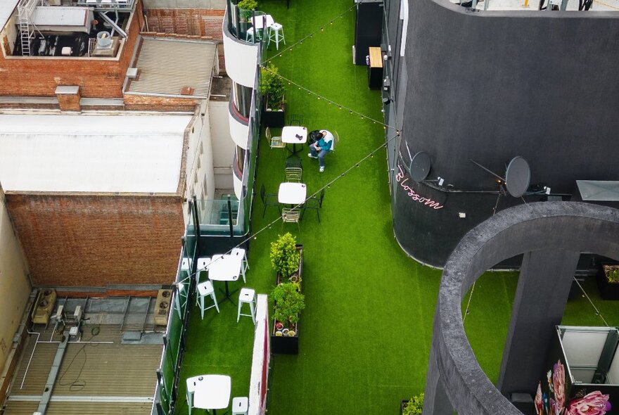 View of astroturf hotel rooftop with tables and chairs.