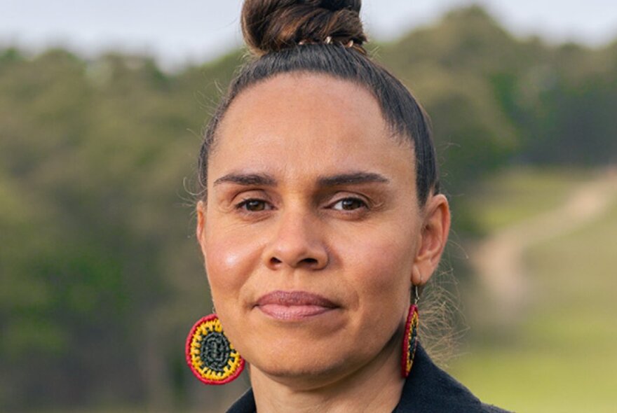 Woman with her hair in a topknot and Indigenous-coloured macrame earrings in an outdoor setting.