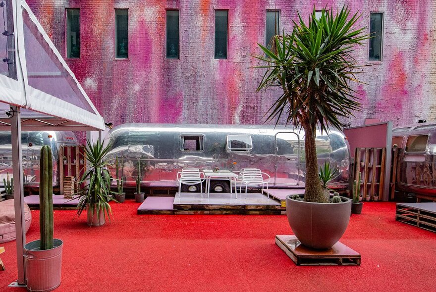A silver caravan decked out as a hotel on a red and pink rooftop.