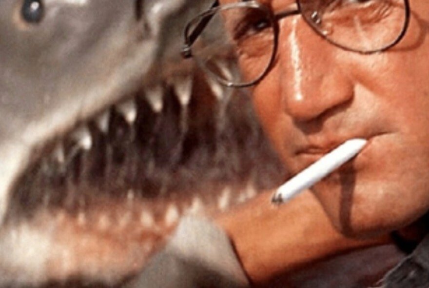 Still from the film, Jaws, with a close-up of an actor smoking a cigarette, with a shark's open jaws right behind him.