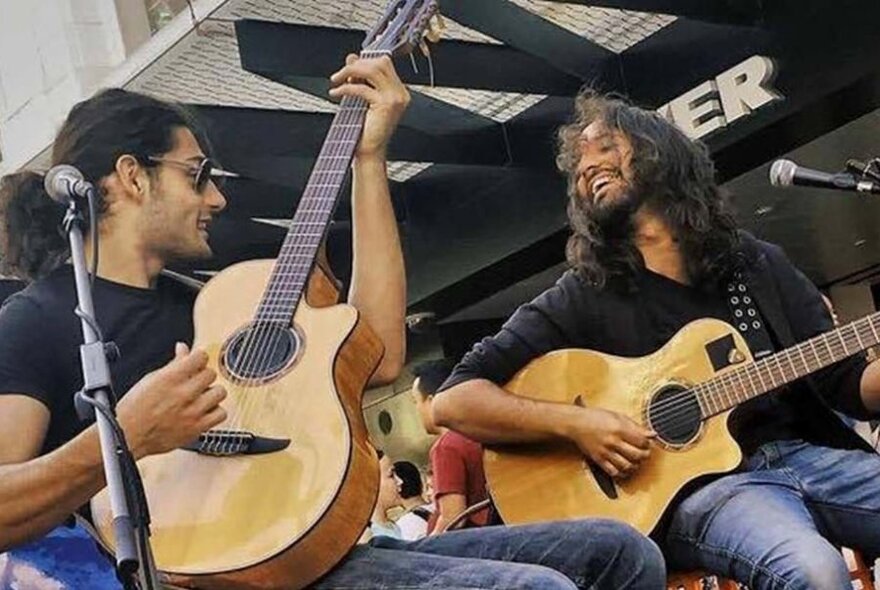 Two men in black shirts and jeans playing acoustic guitar outside the front of MYER store in the Bourke Street mall.