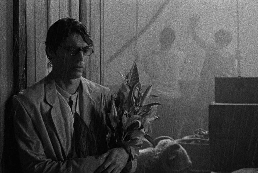 Black and white film still of a man wearing a suit and holding a bunch of flowers.