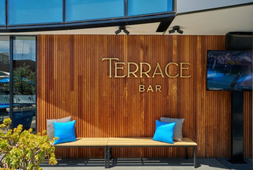 Signage that reads Terrace Bar with a long bench seat and blue cushions underneath the lettering.