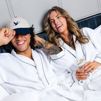 A laughing couple wearing white bath robes lying on a bed in a room at the W Melbourne.