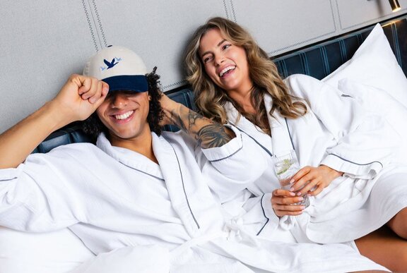A laughing couple wearing white bath robes lying on a bed in a room at the W Melbourne.