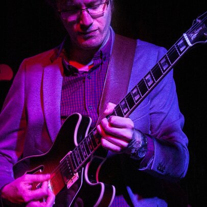 Jazz guitarist Lee Jones playing guitar under a purple light.