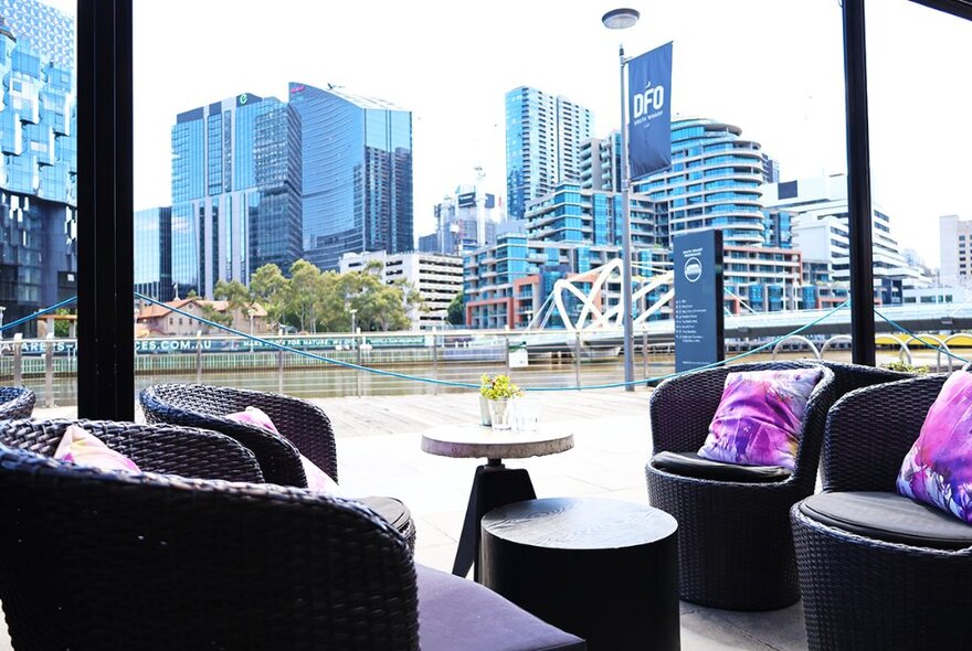 Seating area with chairs and tables beside huge floor to ceiling windows with views of the Yarra and city buildings.