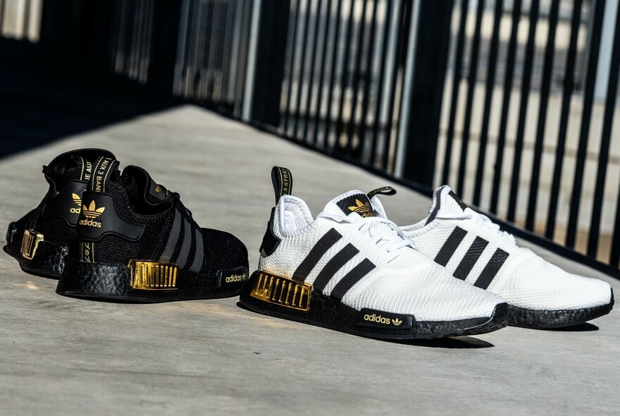 A black and a white pair of classic three-stripes Adidas trainers arranged on concrete.