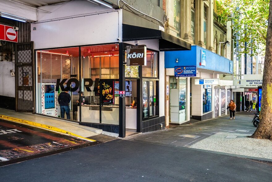 A small ice cream shop on a city corner next to the driveway of a carpark.