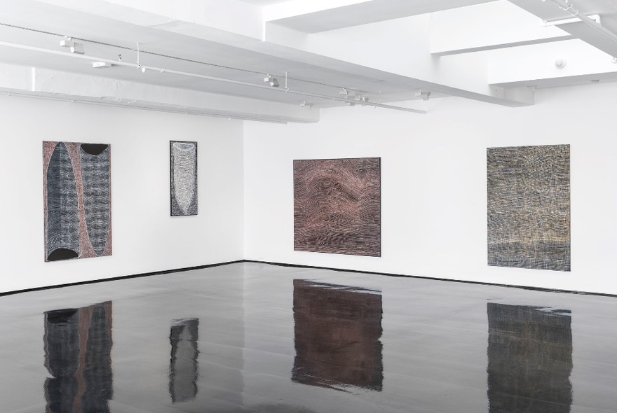 Four contemporary paintings hanging on two white walls in a gallery space.