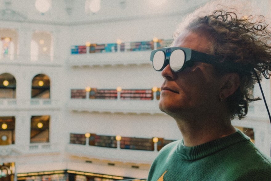 Person wearing virtual-reality glasses in State Library Victoria's upper level Dome with mezzanine aisles and arches.