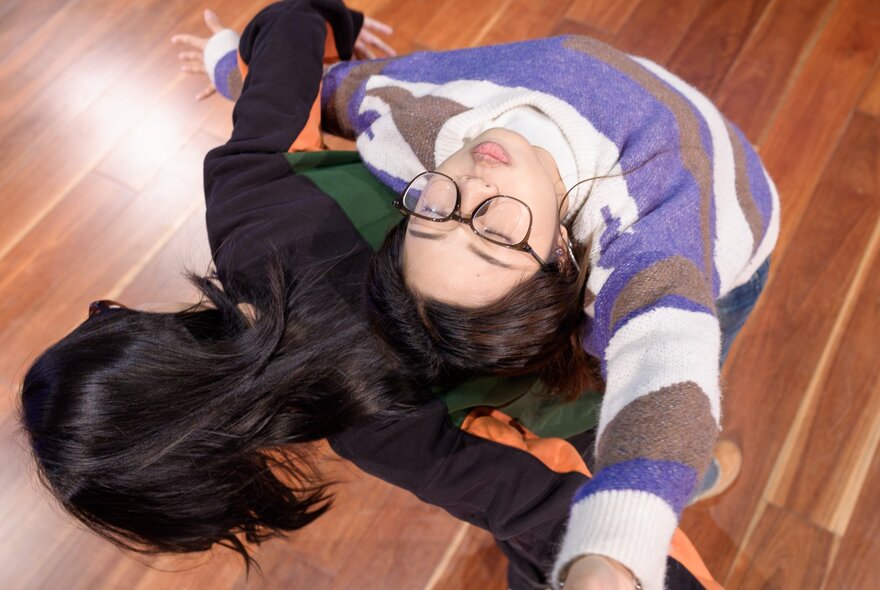 Looking down on two women dancing back to back, one with her head facing the ceiling. 