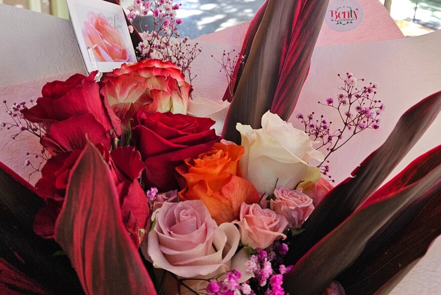 A red-toned bouquet of roses nestled within red-toned snake plant leaves.
