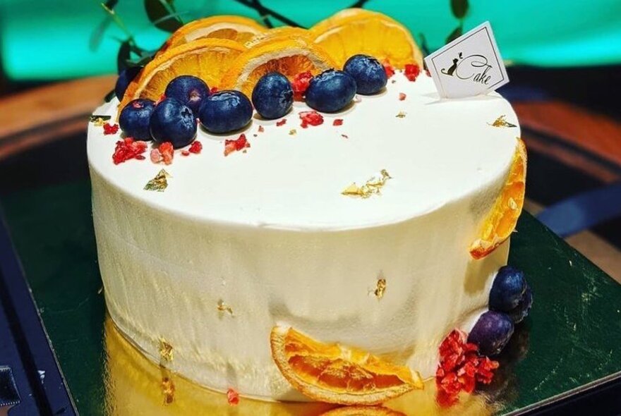 Oranges and blueberries decorating an iced cake.