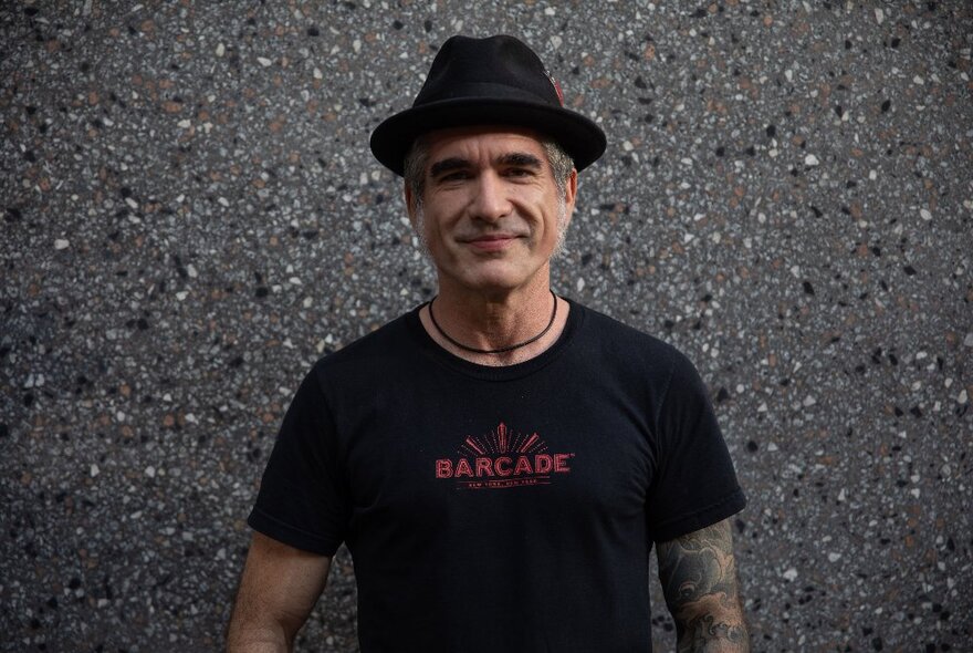 Singer and musician Jack Jones wearing a pork pie hat and black t-shirt against a speckled background. 