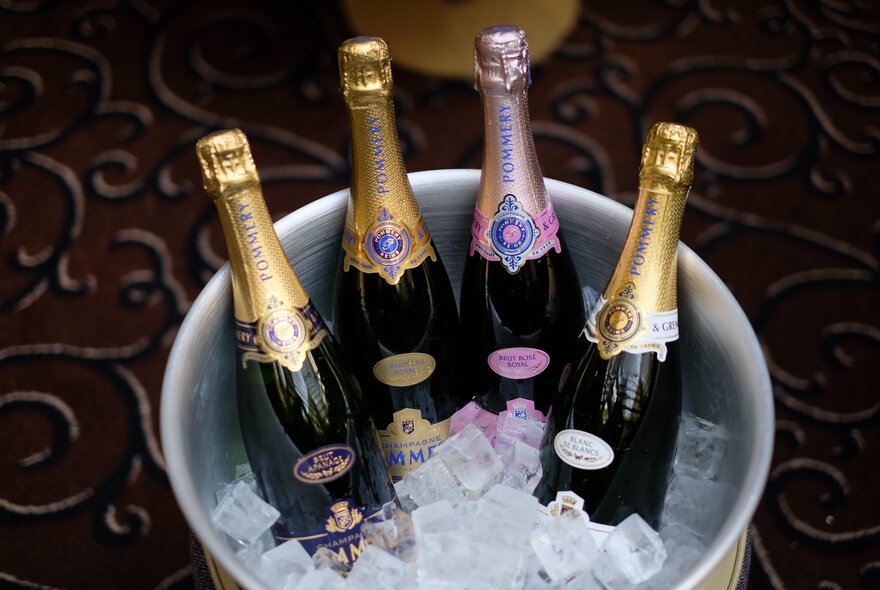 A champagne bucket filled with one pink-topped and three gold-topped champagne bottles in ice.