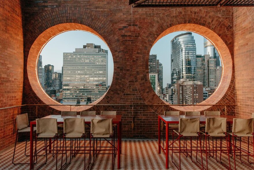 Terrace dining tables with circular window views of city buildings.