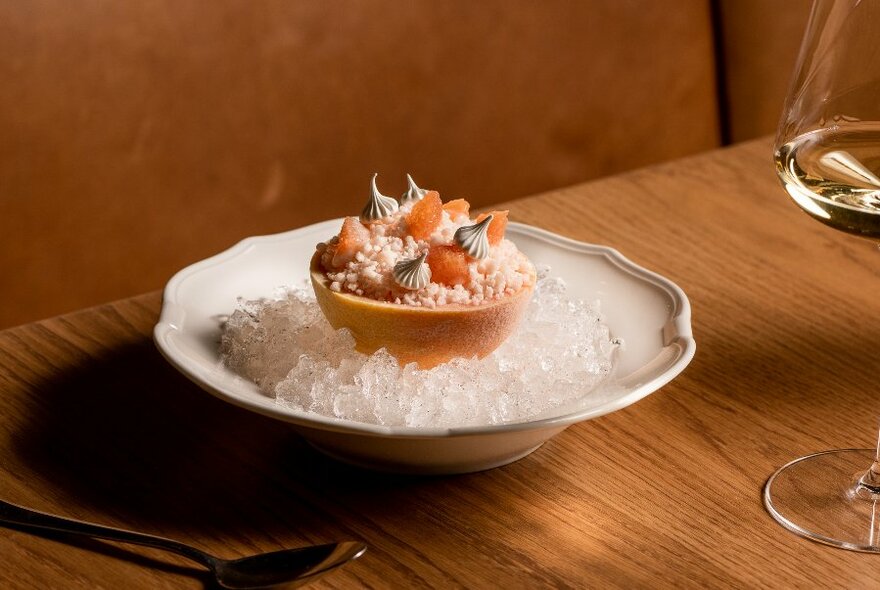 Food carefully arranged in a bowl of ice on a sleek dining table, a glass of wine in the right of the frame.