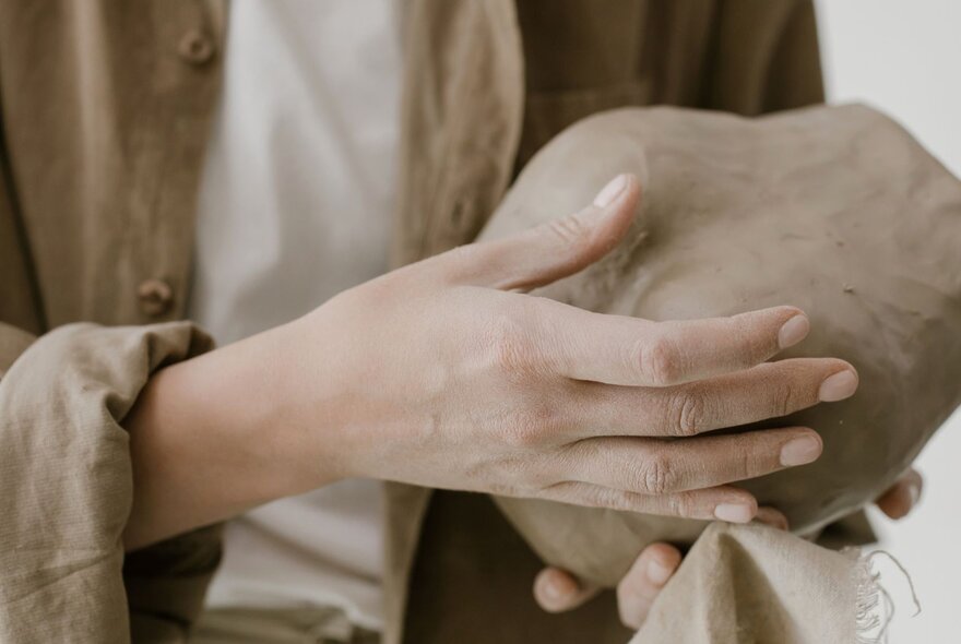 Hands holding a large ball of clay.