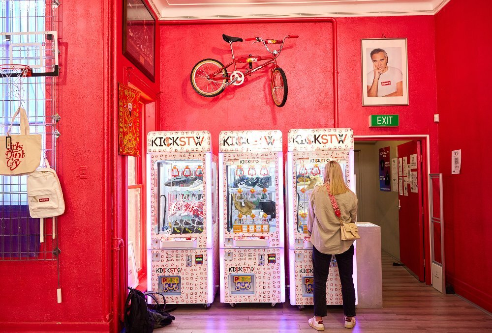 A woman is playing with a vending machine in a streetwear shop with bright red walls.