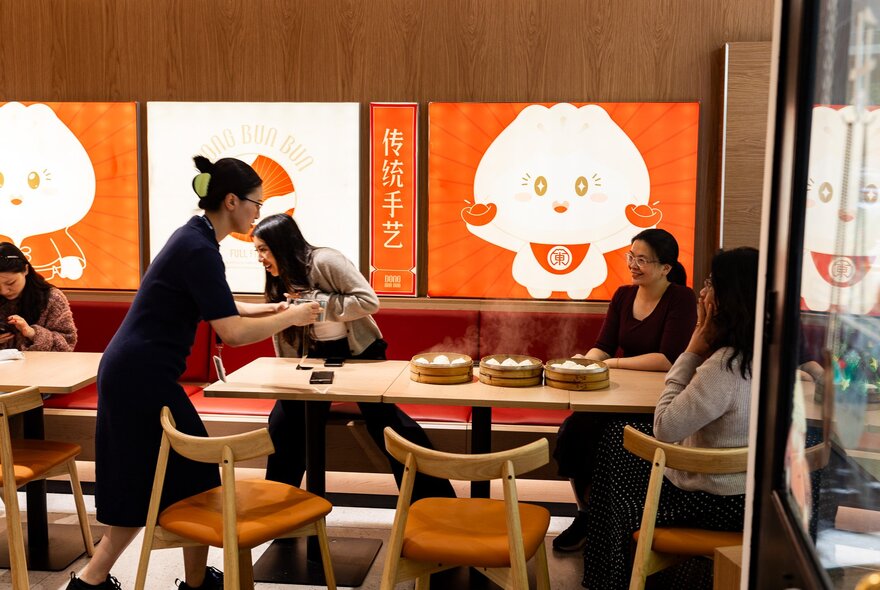 Person serving dumplings to diners at a table in a dumpling bar.
