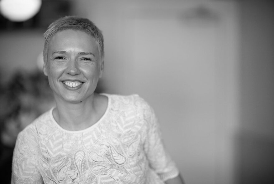 Smiling woman with very short hair, wearing a white top.