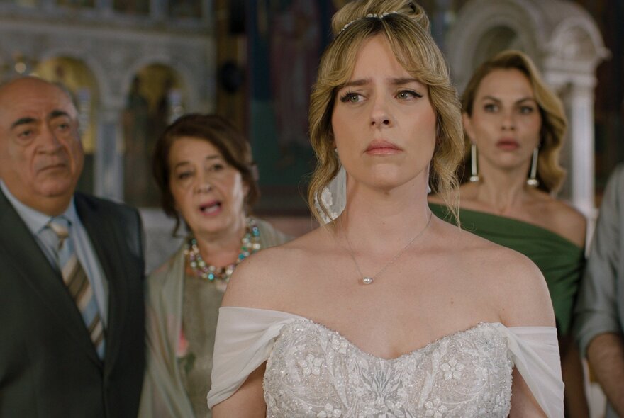 A still from a movie showing an actress dressed as a bride with three people behind her, all looking pensive.