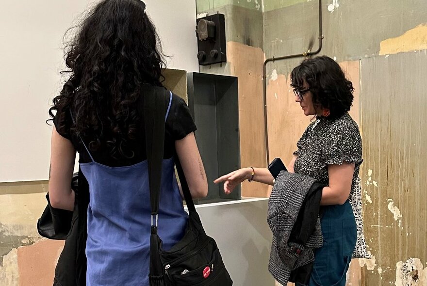 Two people in a run-down looking studio space, pointing and talking. 