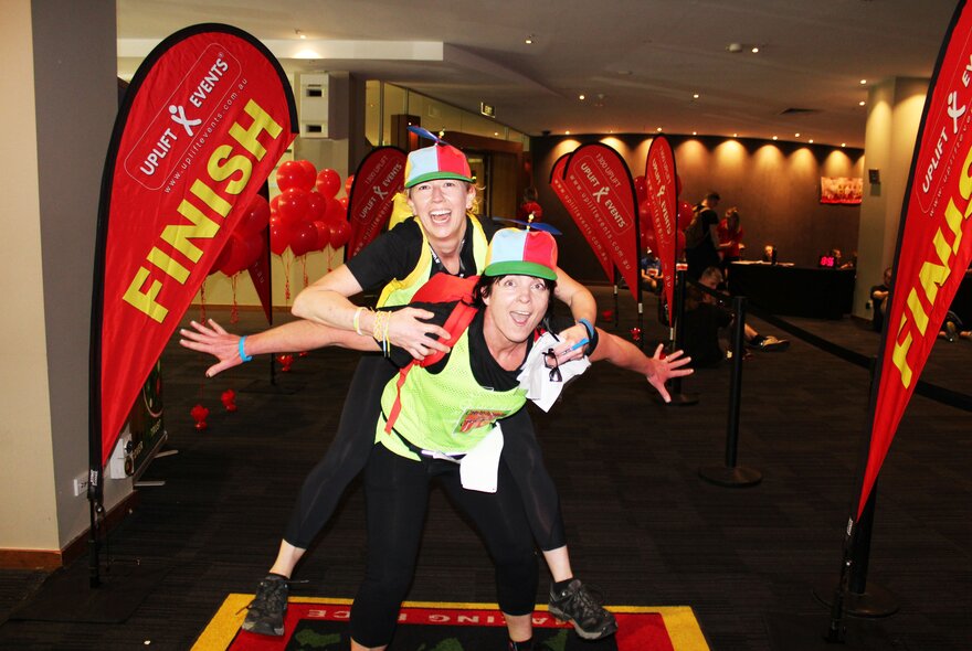 A person being piggybacked by another at a small finish line with red flags. 